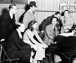 L to R: seated: Fred Astaire, Ginger Rogers, George Gershwin; standing: dance director Hermes Pan, film director Mark Sandrich, lyricist Ira Gershwin, and music director Nathaniel Shilkret (1936) 